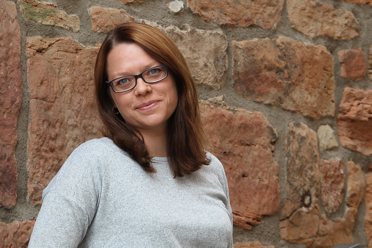 Karina Scholz bietet Pressearbeit für Verbände im Gesundheitswesen und lächelt im hellgrauen Pulli in die Kamera.