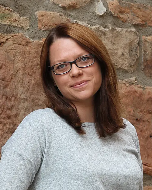 Karina Scholz bietet Pressearbeit für Verbände im Gesundheitswesen und lächelt im hellgrauen Pulli in die Kamera.
