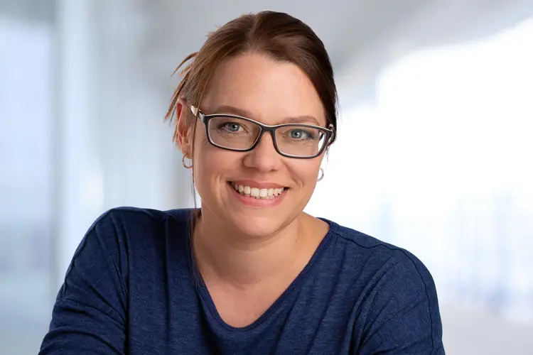 Karina Scholz spricht auf der Über mich Seite über ihre Motivation, Geschichten & Themen so zu erzählen, dass Menschen sie gerne lesen, sehen und hören und lächelt dabei im dunkelblauen Pulli für die Über mich-Seite in die Kamera.