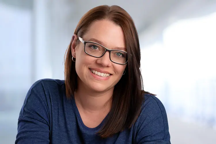 Karina Scholz spricht über ihre Motivation, Geschichten & Themen so zu erzählen, dass Menschen sie gerne lesen, sehen und hören und lächelt dabei im dunkelblauen Pulli für die Über mich Seite in die Kamera.